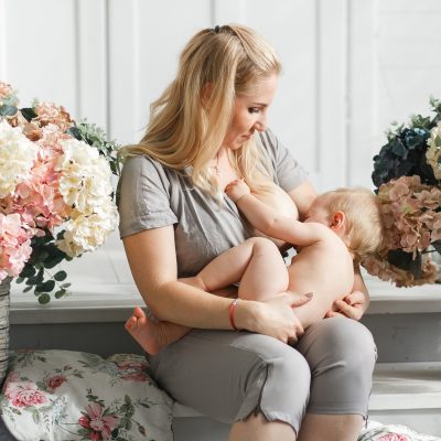 Mother holding baby on her laps before breastfeeding. Studio shot in flowers decor.