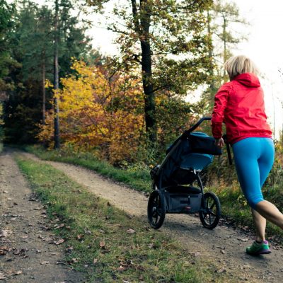 Running mother with child in stroller enjoying motherhood at autumn sunset and mountains landscape. Jogging or power walking woman with pram in woods. Beautiful inspirational mountains landscape.