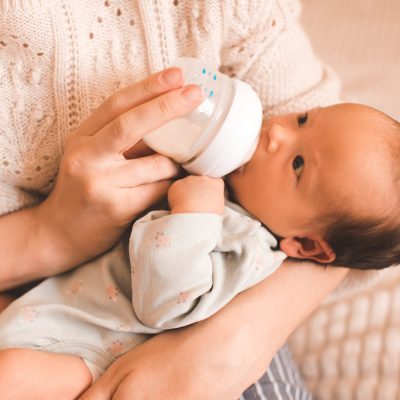 Woman feeding baby infant girl with milk in bottle wear casual clothes in bedroom on mother hands closeup. Motherhood. Maternity. Healthy nutrition eating.