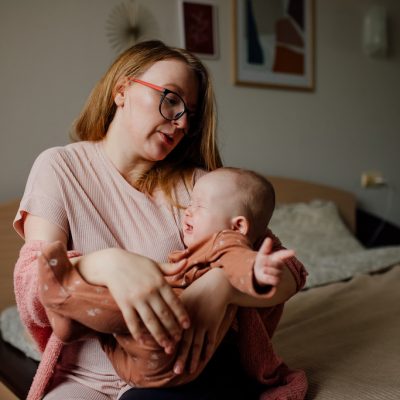 Young mother holding crying baby 6-8 months old, gently touches the baby, Parenthood, trust and protection concept